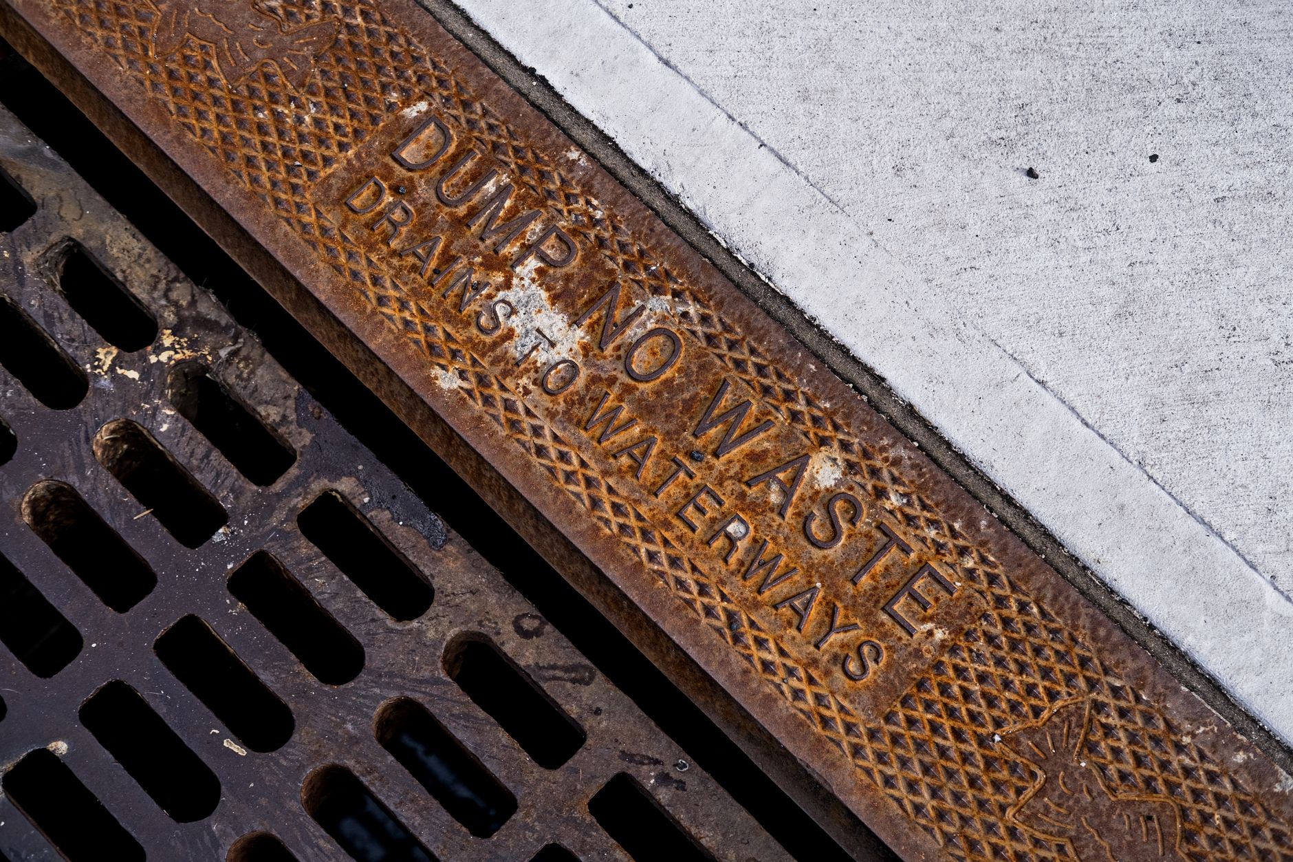 Gros plan d'une grille de drainage rouillée avec un texte d'avertissement environnemental sur un trottoir en béton.